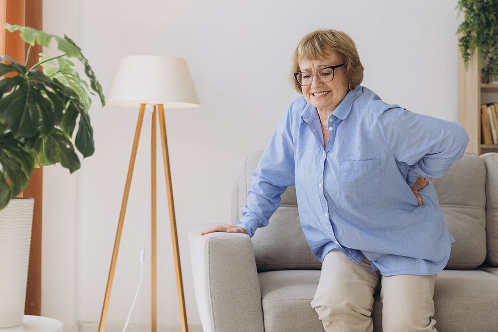 Mature woman with floor dysfunction holding the side of her abdomen while rising off the couch