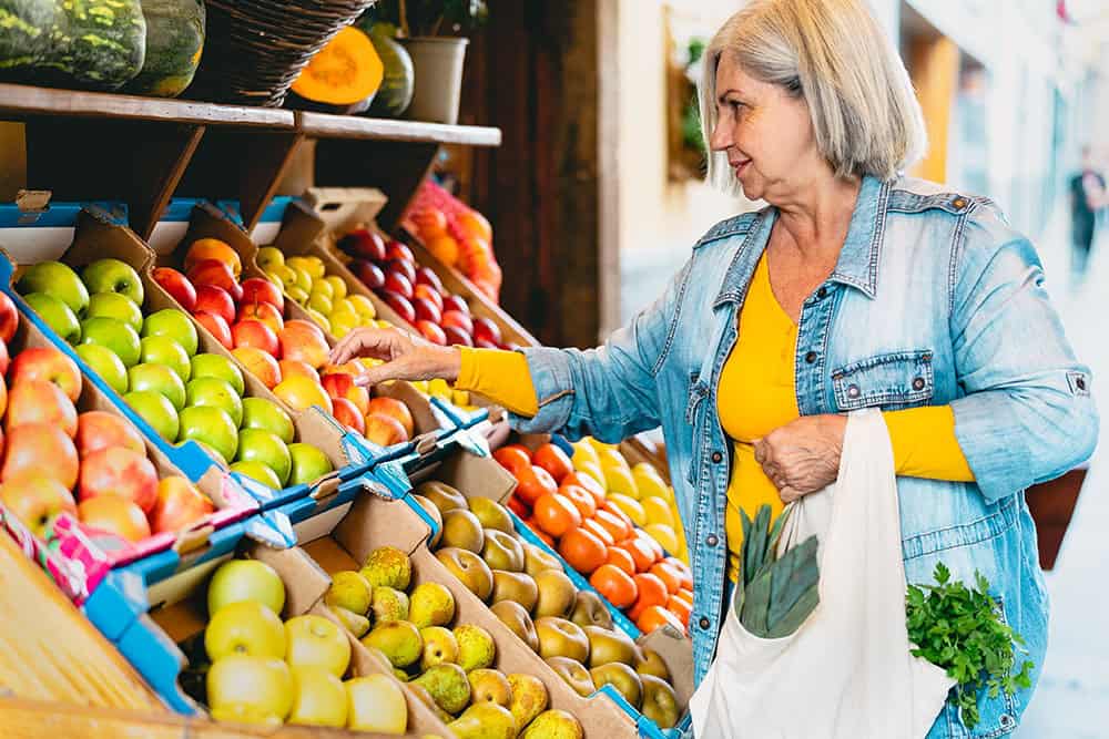Senior woman shopping independently at a market picking out fruit