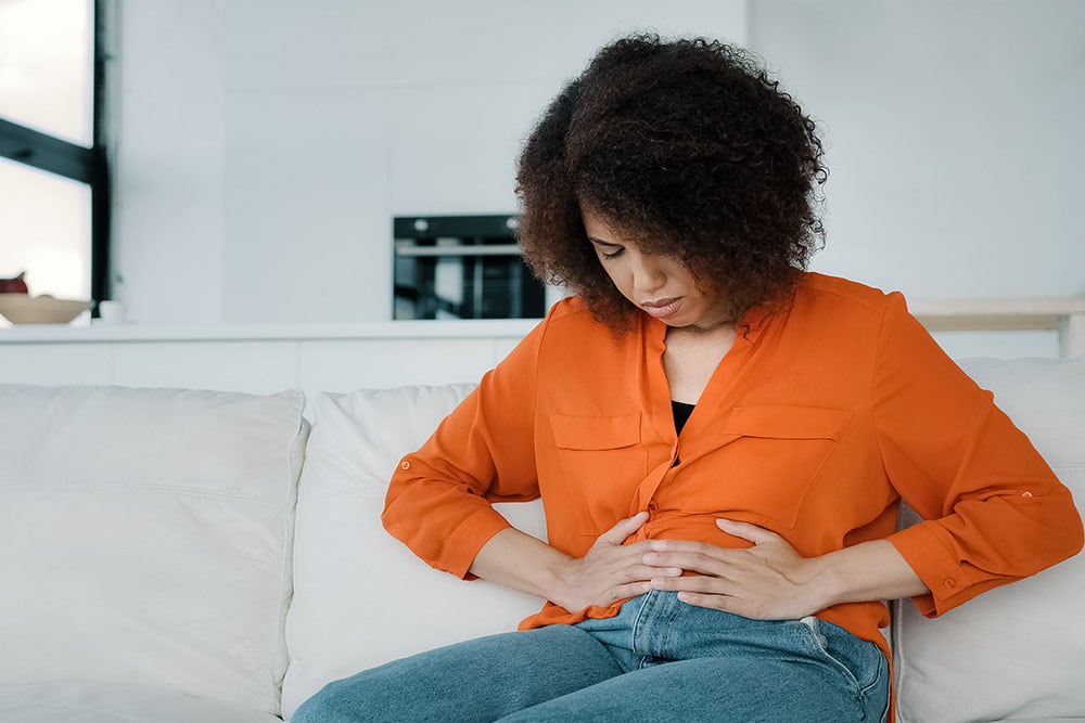 Young African American woman holding her abdomen sitting on a couch